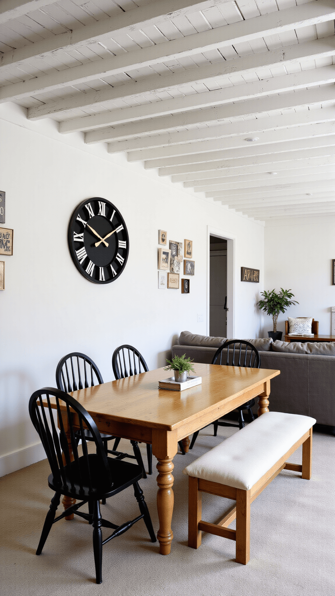 Open-concept space featuring massive whitewashed ceiling beams, distressed pine farmhouse dining table, mixed seating with Windsor chairs and linen-upholstered bench, vintage metal signs on gallery wall, and an oversized black metal clock.