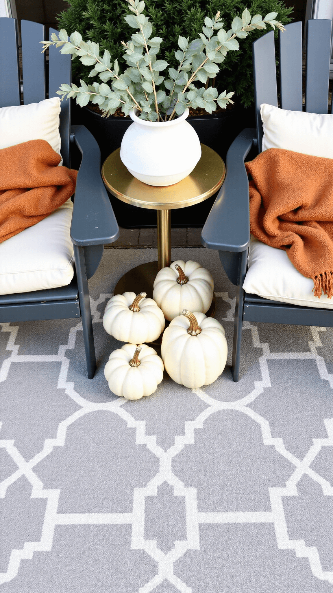 Overhead view of a cozy transitional porch with autumn decor, including Adirondack chairs with cream cushions, white pumpkins, a round metal side table with a vase of dried oak branches and eucalyptus, all over a gray and ivory geometric rug.