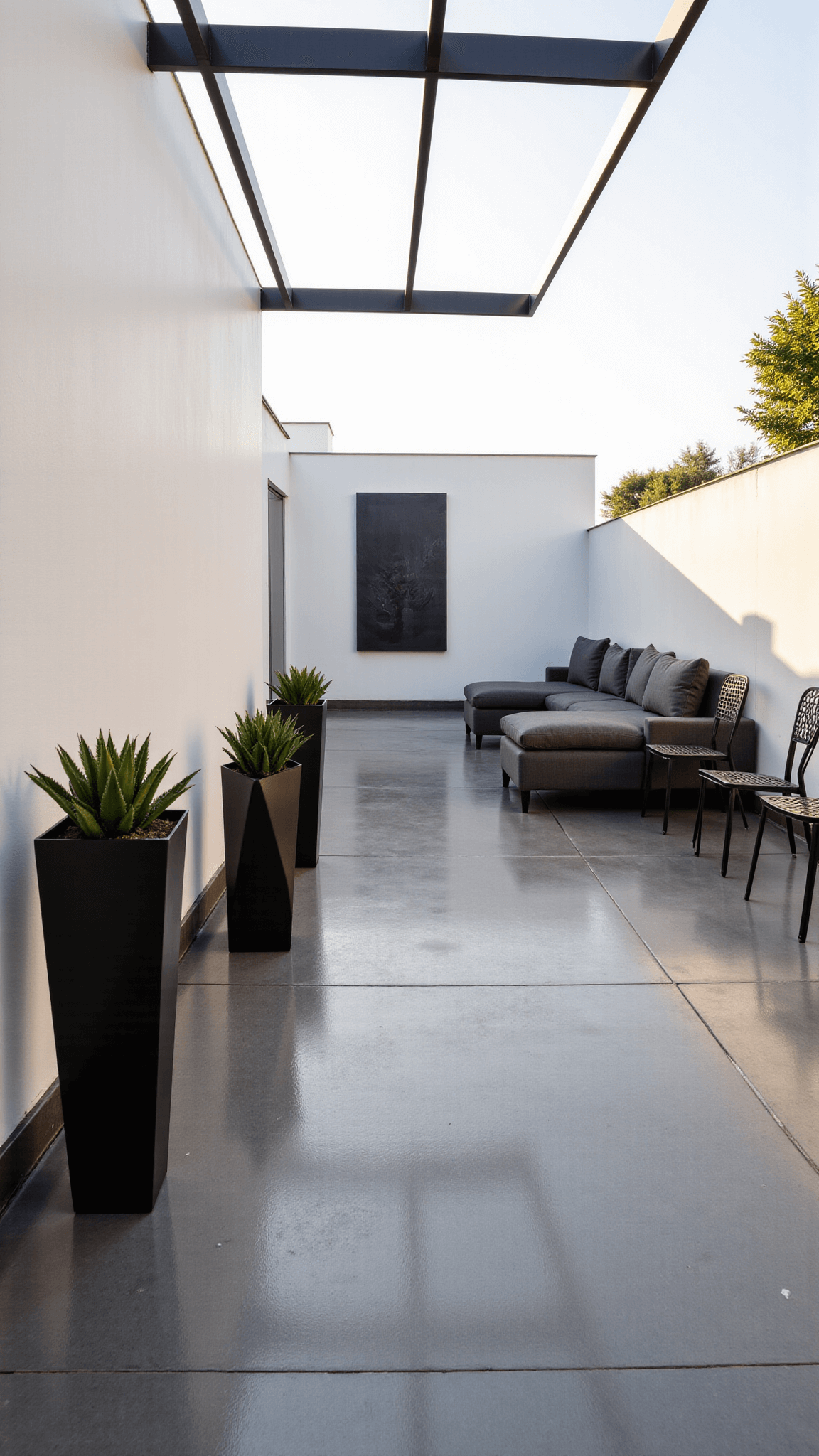 Modern minimalist courtyard with concrete flooring, white 12ft walls, charcoal L-shaped sofa, black metal chairs, geometric planters, and a steel pergola casting dramatic golden hour shadows.