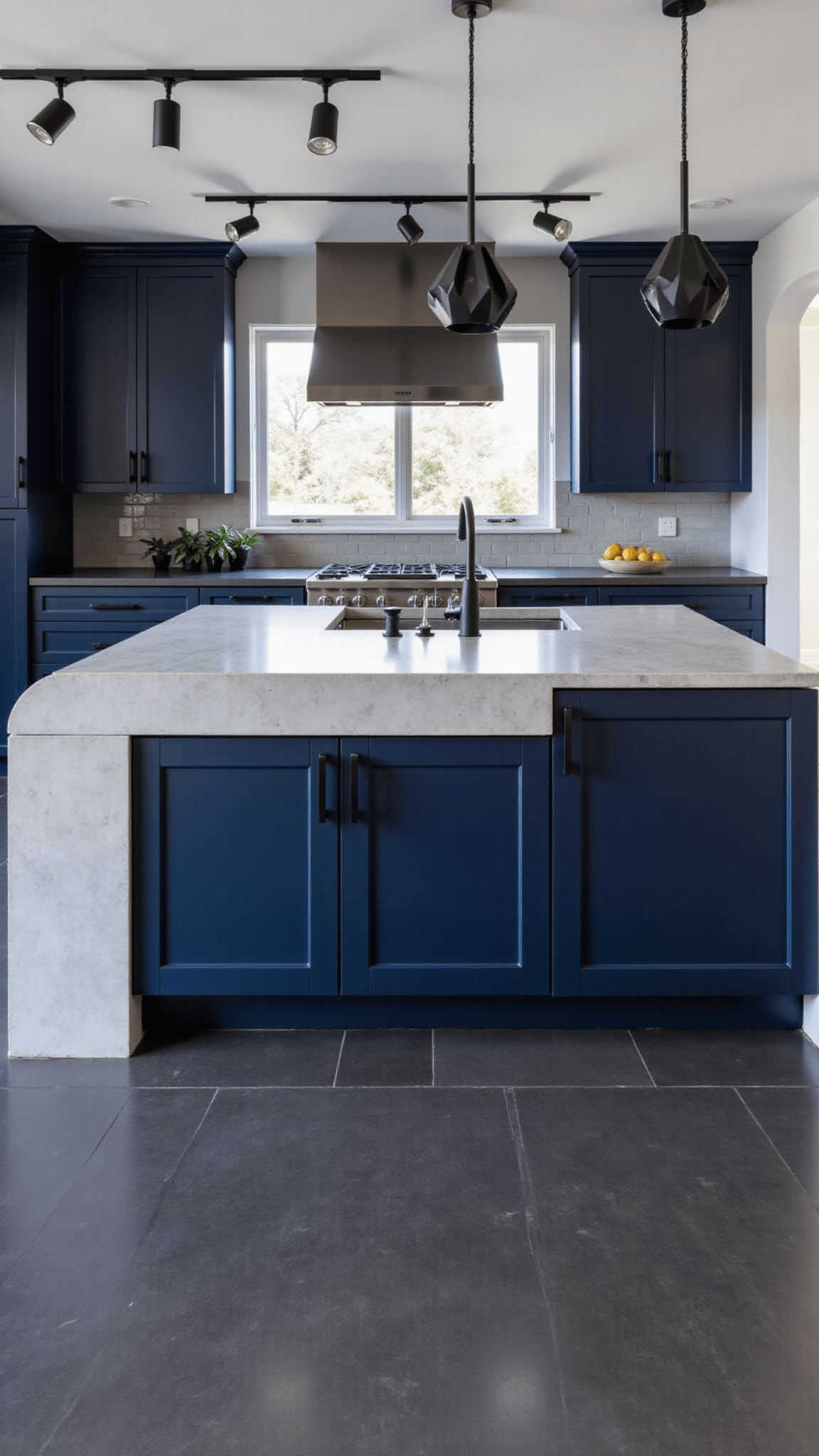 Open-concept kitchen with sleek navy cabinets, concrete countertops, geometric pendant lights in matte black, and large-format charcoal floor tiles, with a bold, architectural atmosphere.