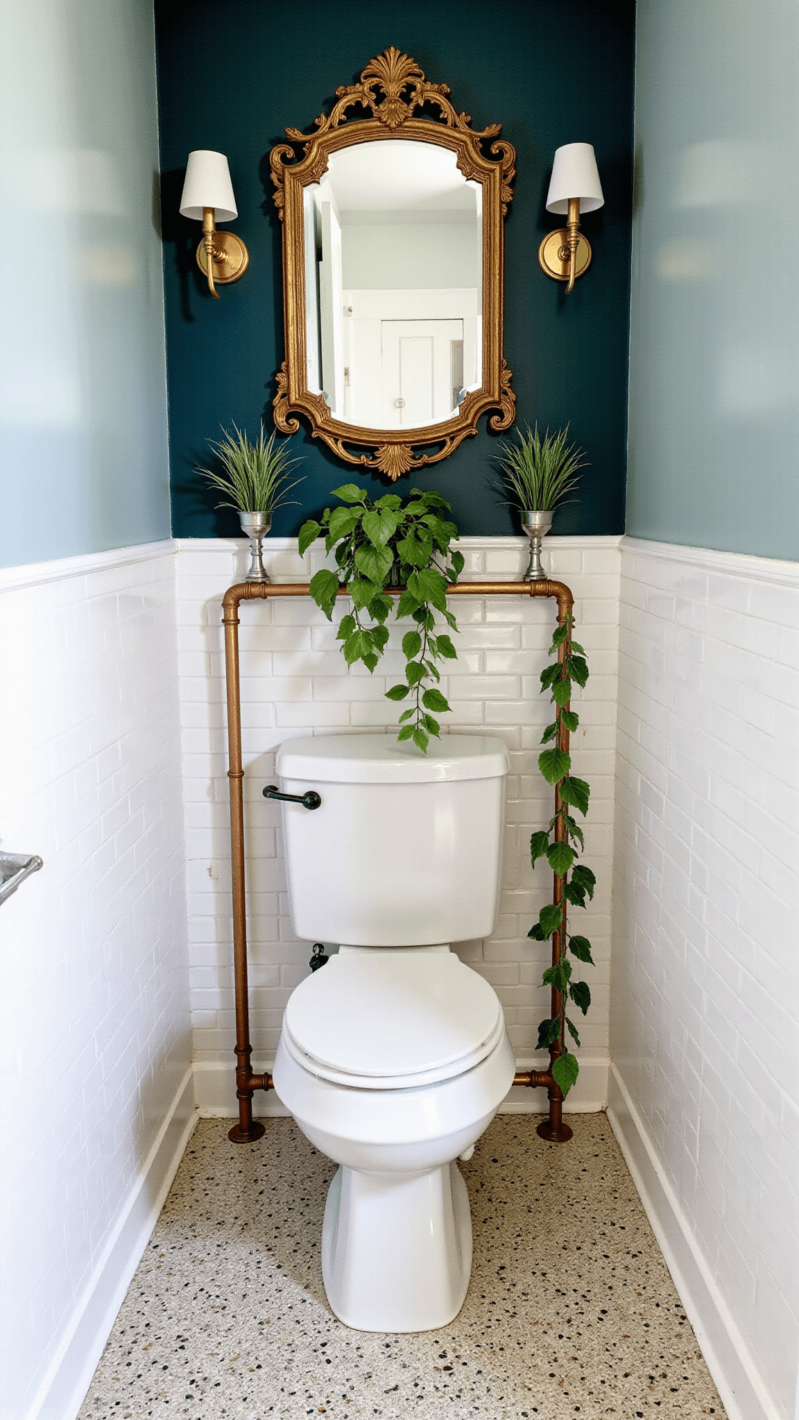 Overhead shot of an intimate powder room with vintage brass sconces, ornate mirror, air plants on a dark teal accent wall, a trailing pothos on copper pipe shelves, white subway tiles and terrazzo flooring.